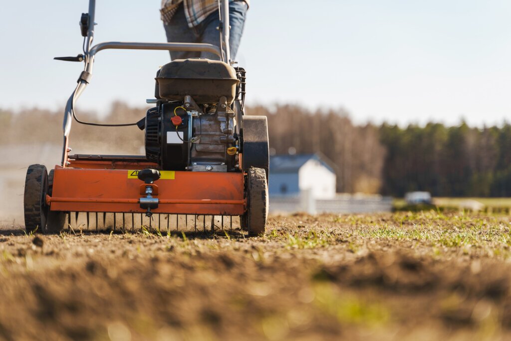 A close-up of a motor-driven core aerator machine on dry, light brown soil, illustrating the seasonal timing involved in the question of how often should you aerate your lawn.
