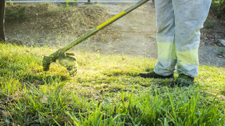 Person wearing safety gear while mowing the lawn, with only their legs visible, emphasizing the importance of safety precautions during lawn maintenance