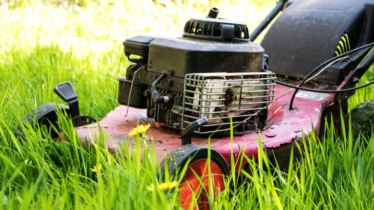 An old lawn mower abandoned in a field of high, uncut grass, symbolizes common lawn mower starting issues discussed in the article