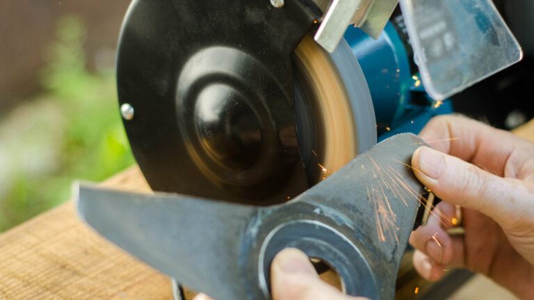 A person meticulously sharpening a lawn mower blade, demonstrating the process described in the guide for achieving a perfectly manicured lawn