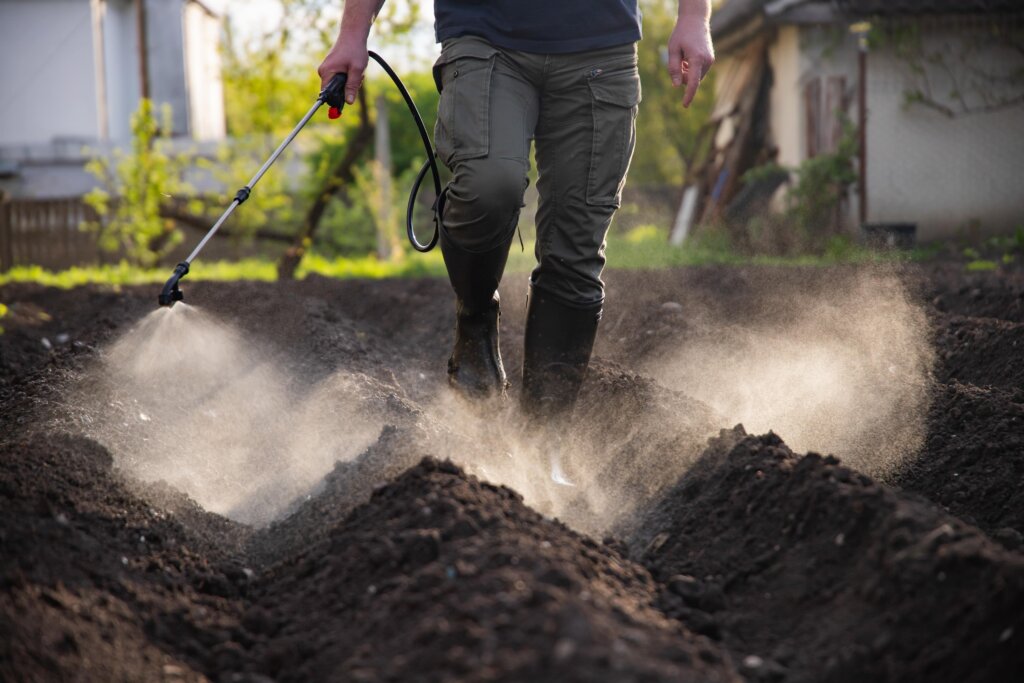 A person spraying liquid from a wand onto tilled, dark soil, illustrating the rapid application and immediate effect of fast release fertilizer.