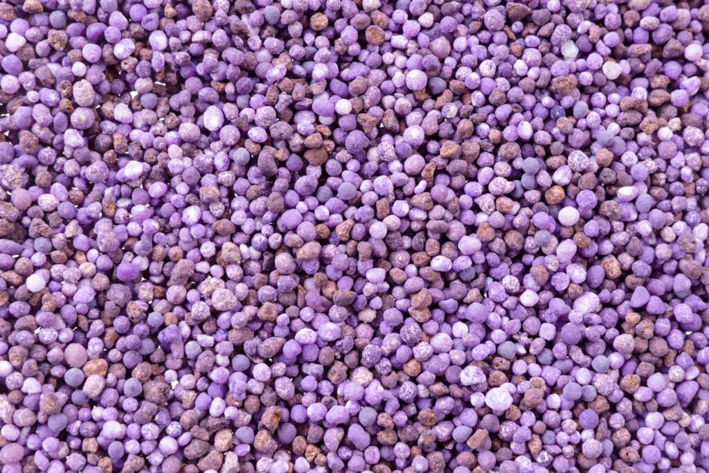 A close-up, full-frame image of purple and brown granular fertilizer pellets, representing the dry methods of fertilizer application.