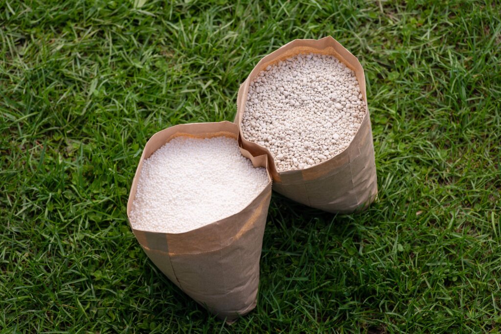 An overhead view of two brown paper bags filled with different types of granular fertilizer, emphasizing the encapsulated nature of slow release fertilizer.