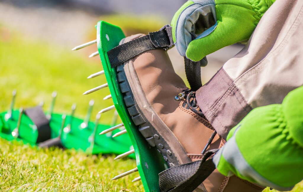 A close-up of a person's foot adjusting a strap on a shoe-mounted spike aerator, illustrating a manual method for how to aerate lawn.