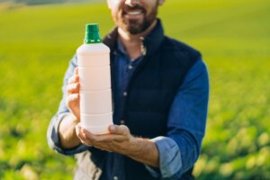A man holding a white bottle of liquid fertilizer in a field of green plants, highlighting the convenience of liquid lawn fertilizer.