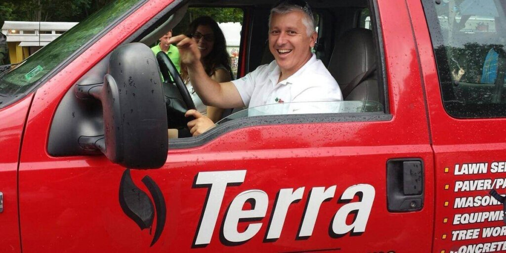 A smiling man in a Terra branded truck holds up a set of keys, with a coworker in the passenger seat behind him