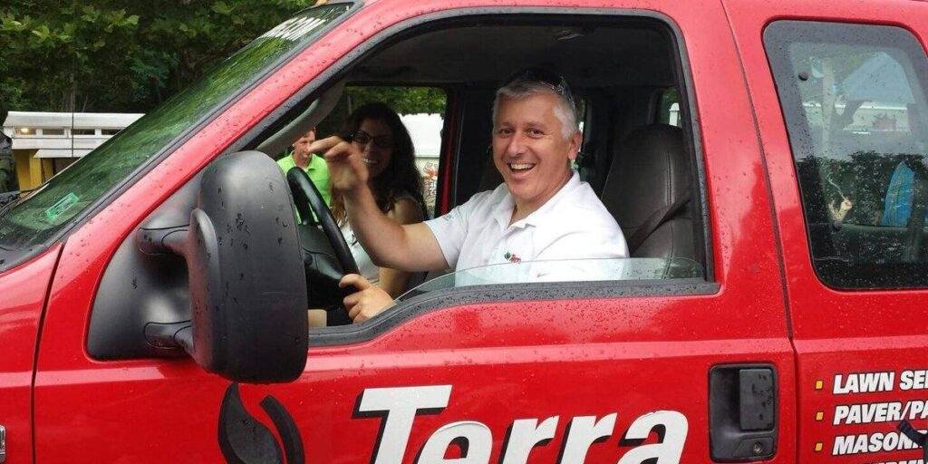 A smiling man in a Terra work shirt leaning out the window of a red company truck.